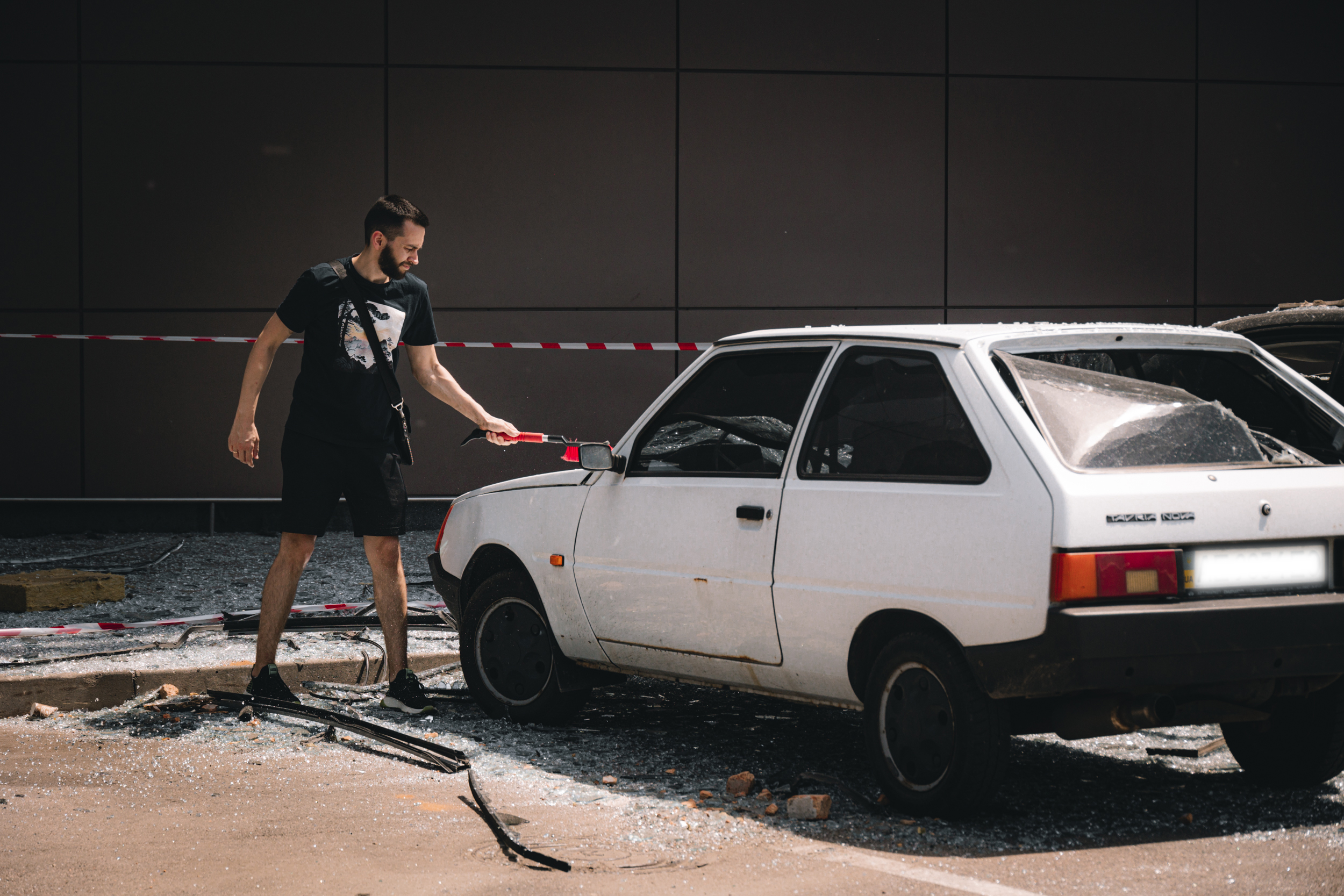 Працівник ТРЦ Артем прибирає скло на своїй знищеній машині