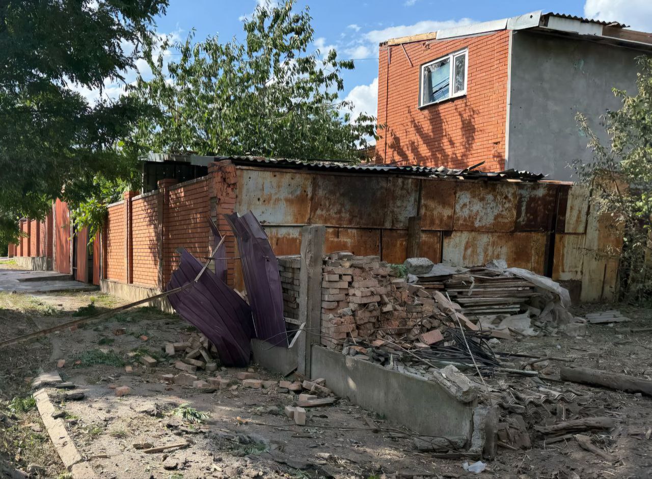 У двоповерховому будинку розбите вікно, поряд - понівечений паркан. 