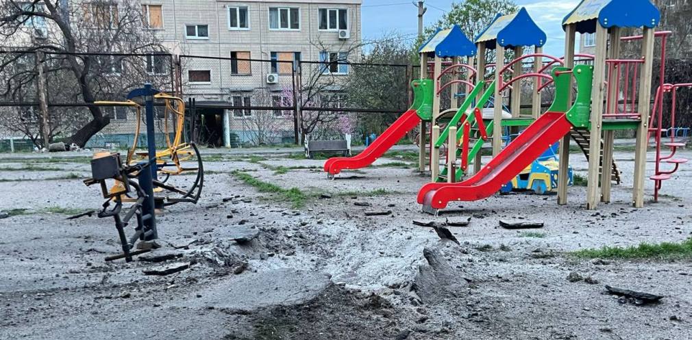 Пошкоджена багатоповерхівка на фоні дитячого майданчика